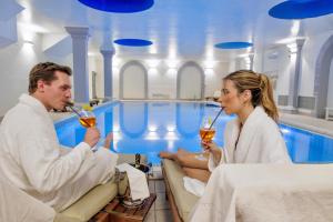 a man and woman drinking wine in front of a swimming pool at Greif Hotel & Spa in Trieste