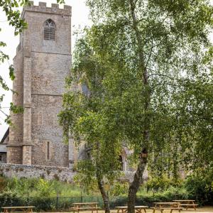 a building with a tower with a tree and benches at The Three Swallows Cley in Cley next the Sea
