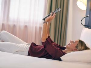 a woman laying on a bed reading a book at Mercure Paris La Défense in Courbevoie