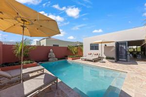 a swimming pool with an umbrella and chairs and a house at Casa Carpe Diem with private pool, Mambo Beach in Willemstad
