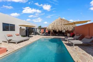 a pool with chairs and umbrellas next to a house at Casa Carpe Diem with private pool, Mambo Beach in Willemstad