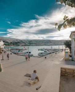 um homem sentado em um banco em um píer perto da água em Stone House 4M - Stylish Coastal Stay with 3 Ensuites & Parking, Pag em Pag