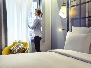 une femme qui regarde par la fenêtre dans une chambre d'hôtel dans l'établissement Mercure Paris la Défense Grande Arche, à Nanterre
