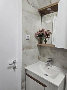 a bathroom with a sink and a mirror and flowers at Apartman Karamelica in Užice