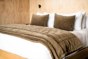 una cama grande con sábanas blancas y almohadas marrones en Tukare Lookout, en Te Anau