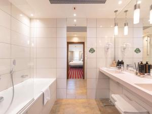 a white bathroom with two sinks and a tub at Mercure Warszawa Grand in Warsaw