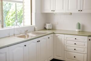 een keuken met witte kasten, een gootsteen en een raam bij Bombo Beach House in Kiama +23 foto's