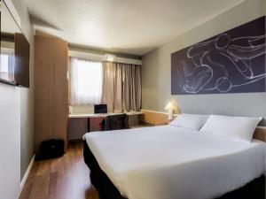 a hotel room with a large white bed and a desk at Ibis Granada in Granada +106 photos