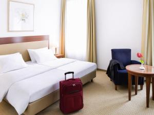 a hotel room with a bed and a red suitcase at Novotel Hildesheim in Hildesheim