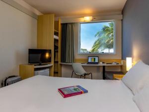 a hotel room with a bed and a desk and a window at ibis Vitoria Aeroporto in Vitória