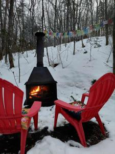 two red chairs and a fireplace in the snow at Yourte Voyageuse in Charette