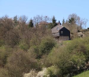 an old barn on a hill with trees and bushes at Kleines Vulkaneifelhaus in Schutz