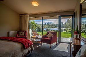 une chambre avec un lit et des chaises et une grande fenêtre dans l'établissement Wilderness Lodge Lake Moeraki, à Haast