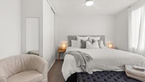 a white bedroom with a large bed and a chair at Seaview 5 - Great Beach Views in Avoca Beach +9 photos