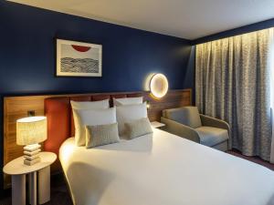 a hotel room with a large bed and a chair at Mercure Caen Cote De Nacre in Caen