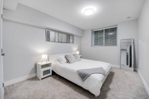 a white bedroom with a bed and two windows at Spacious 1BR Suite Near Capilano Bridge & Trails in North Vancouver