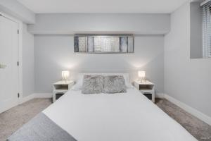 a white bedroom with a bed and two night stands at Spacious 1BR Suite Near Capilano Bridge & Trails in North Vancouver