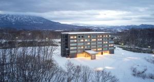 un edificio en la nieve con montañas en el fondo en Hinode Hills Niseko Village, en Niseko