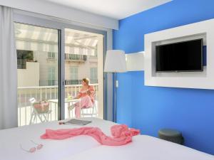 ein Zimmer mit einem Bett und einer Frau, die auf einem Balkon sitzt in der Unterkunft Ibis Styles Menton Centre in Menton