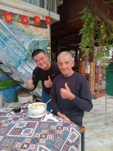 two men giving thumbs up at a table with a bowl of food at An' Home Mai Chau in Mai Chau