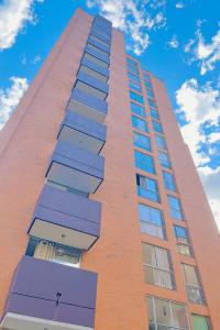 Un alto edificio de ladrillo con ventanas moradas y un cielo azul en ApartaSuite 2 a 3 personas cerca club campestre, en Medellín