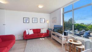 a living room with a red couch and a large window at Seaview 7 - Prime Position Beachside Holiday in Avoca Beach