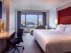 a hotel room with a bed and a desk and a window at Grand Mercure Jakarta Harmoni in Jakarta