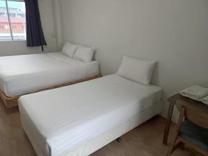 Dos camas en una habitación pequeña con una mesa. en Comfy Hotels Suvarnabhumi Airport, en Samut Prakan