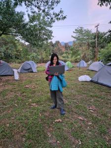 una mujer sosteniendo una computadora portátil frente a un grupo de tiendas de campaña en Safarnama Hornbill Camping near festival ground, en Jāmb