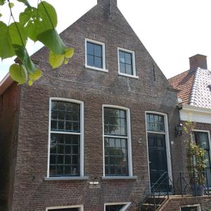a brick house with four windows and a black door at De olde banck in Stavoren