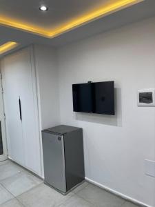 Ein Fernseher an einer weißen Wand neben einem Kühlschrank in der Unterkunft Studio Chic in Mahdia