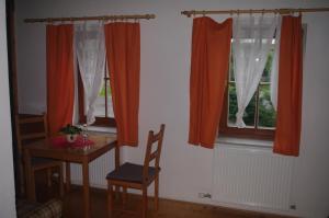 a room with two windows with orange curtains and a table at Penzion Avalanche in Železná Ruda