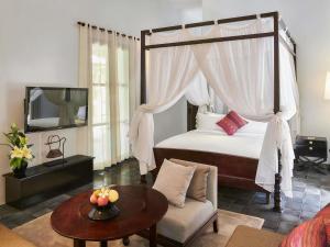 a bedroom with a canopy bed with a table and a couch at Sofitel Luang Prabang in Luang Prabang