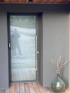 MontcelStudio Boheme Chic I Vue Panoramique Montagnes I Calme Absolu的一个人站在玻璃门后，手里拿着一个花瓶。