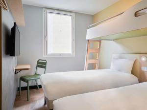 a bedroom with two beds and a chair and a window at ibis budget Saint-Maurice in Saint-Maurice