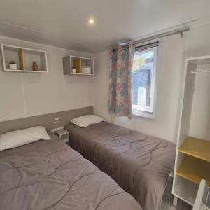 two beds in a small room with a window at EL Miya Sol Mobil Home à 200m de la Plage in Torreilles