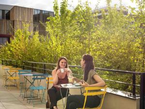 two women sitting at a table with a cup of coffee at Aparthotel Adagio access Colombes La Défense in Colombes