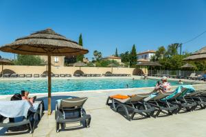 Un grupo de personas sentadas en sillas junto a una piscina. en Camping maeva Escapades Le Hameau des Pins, en La Crau