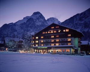 a large building in the snow in front of a mountain at Bernerhof Swiss Quality Hotel in Kandersteg