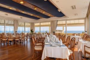 Un restaurante con mesas y sillas blancas y ventanas. en Hotiday Cecina Mare, en Cecina