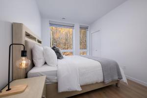 a white bedroom with a bed and a window at Panorama 1253: Two-Level Sanctuary & Views in Petite-Rivière-Saint-François