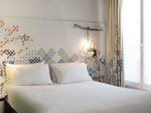 um quarto com uma cama com lençóis brancos e um lustre em Ibis Styles Paris Gare Saint Lazare em Paris