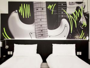 two beds in a room with a guitar on the wall at ibis Styles Taubate in Taubaté