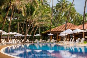 a pool with chairs and umbrellas and palm trees at Jatiúca Suítes Resort - Flat 413 in Maceió