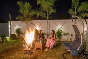 duas mulheres sentadas ao redor de uma fogueira em um quintal à noite em Villa Papillon by DanCenter | Pvt Pool | Jacuzzi | Kids Room | Udaipur em Thūr