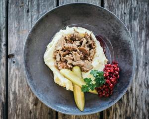 a bowl of food with meat and vegetables on a wooden table at Arctic Lumo Resort in Kuusamo