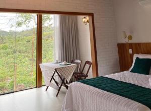 a bedroom with a bed and a table and a window at Chalé Colibri Verde in Santa Teresa