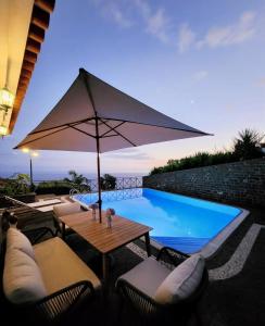 a table with an umbrella next to a swimming pool at Villa Ocean Wave Calheta - Heated Pool & Stunning Ocean View in Calheta