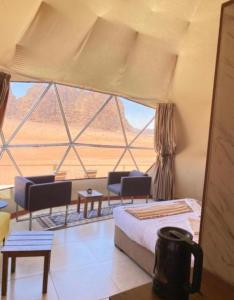 Una habitación con una cama y sillas y una ventana grande. en JULIA RUM lUXURY CAMP, en Wadi Rum