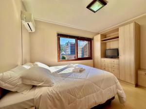 una camera da letto con un grande letto bianco con una finestra di Apartamento no centro de Gramado a Gramado